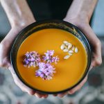 Man's hands holding creamed pumpkin soup garnished with edible flowers, close-up